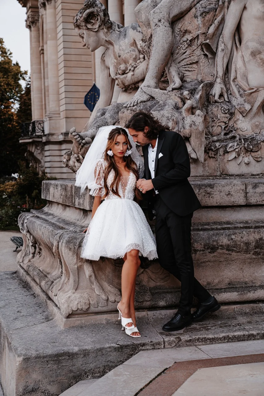 Anais seated at the base of a fountain, Antoine leaning beside her