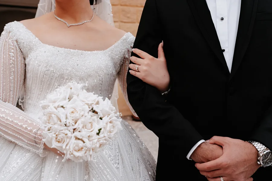 Close-up of the bouquet, the beaded dress and her hand on the groom arm